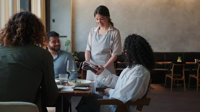 Happy african birthday woman pays by card to waiter for party with multiethnic friends in cafe