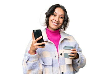 Young Argentinian woman wearing winter muffs over isolated background holding coffee to take away...