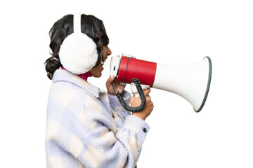 Young Argentinian woman wearing winter muffs over isolated background shouting through a megaphone