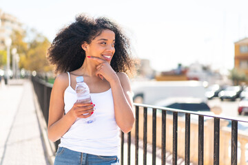 Young African American woman with a bottle of water at outdoors thinking an idea and looking side
