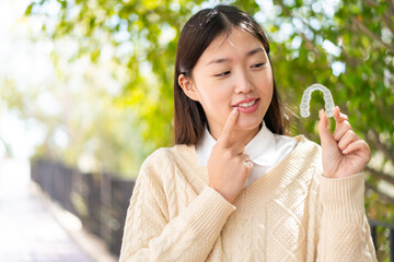 Young Chinese woman at outdoors holding invisible braces with happy expression