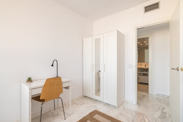 Cozy interior in white tones with wardrobe and table and chair with open door to the bathroom. Concept of a bright new fresh interior in the apartment