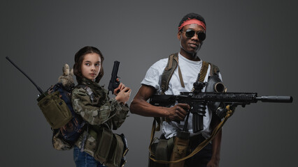 Shot of little girl with handgun and black man with rifle against grey background.