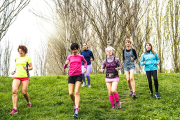 Fototapeta premium Multigenerational women running at the park on a wild grassy path - Group of female runners training outdoors for trail marathon race - Concept of wellness and body care in middle and old age