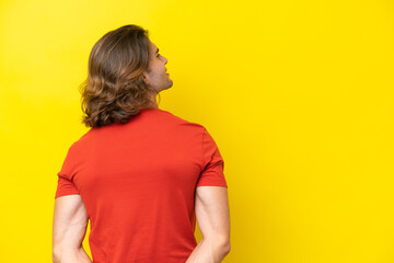 Caucasian handsome man isolated on yellow background in back position and looking back