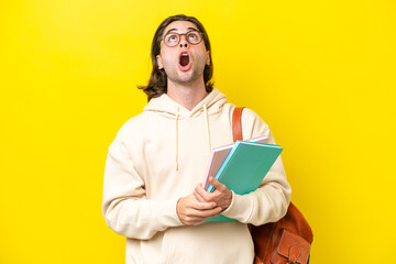 Young student handsome man isolated on yellow background looking up and with surprised expression