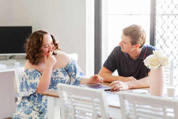 Male NDIS provider assisting young woman with down syndrome using tablet