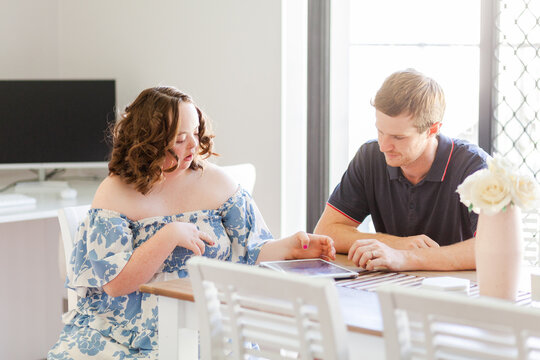 Male NDIS provider assisting young woman with down syndrome using tablet