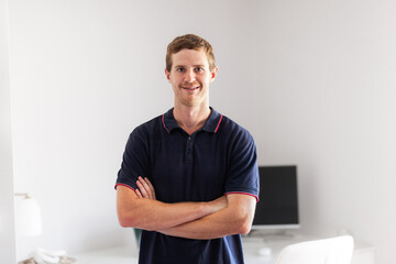 Environmental portrait of young man in his twenties standing with home office behind