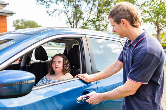 Male NDIS provider assisting young woman with down syndrome getting into car to travel