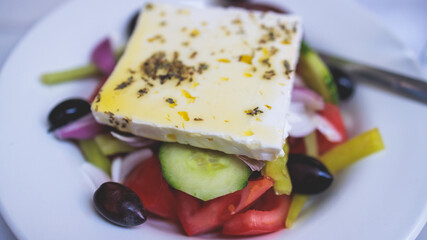 Traditional fresh greek salad with vegetables, feta cheese, spices olives and olive oil on a plate served in traditional Greek cafe tavern restaurant in the street of Athens, Greece