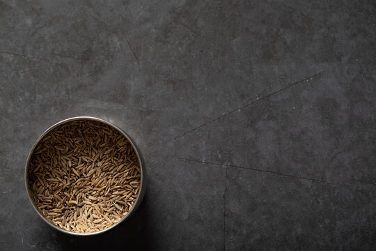 Spice tin of cumin seeds on dark marble background