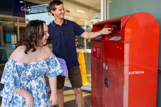 Happy teenager with down syndrome using post office box to send parcel in compostable packaging