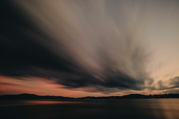Long exposure shot of the gray clouds above a calm sea with the sunset in the background