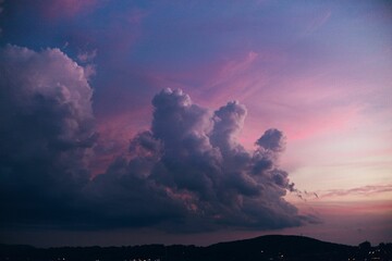 Big white clouds in the pink sunset sky with hill silhouettes underneath