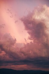 Vertical shot of the big white clouds in the pink sunset sky with hill silhouettes underneath