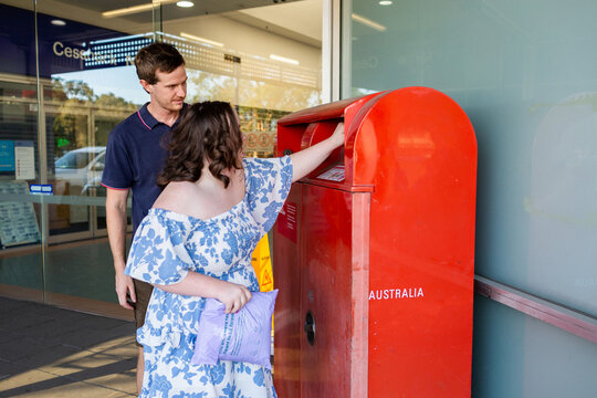 Happy teenager with down syndrome using post office box to send parcel in compostable packaging