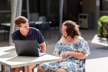 Adult and teenager talking together at outdoor café with laptop open