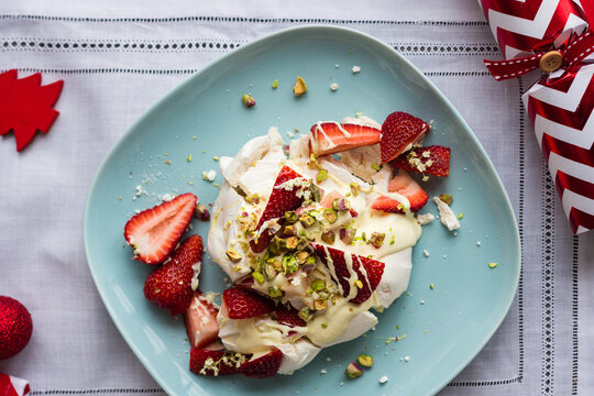 Individual dessert for christmas, a smashed meringue topped with cream, strawberries, pistachio