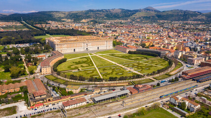 Aerial view of the Royal Palace of Caserta also known as Reggia di Caserta. It is a former royal residence with large gardens in Caserta, near Naples, Italy. The historic center of the city is nearby. - obrazy, fototapety, plakaty
