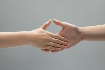 Closeup shot of two helping hands touching in front of a gray background