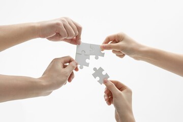 Closeup shot of hands holding puzzle pieces in front of a white background
