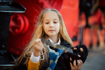 A girl in a robe with blond hair near a red train holds a black mole in her hands. A little...
