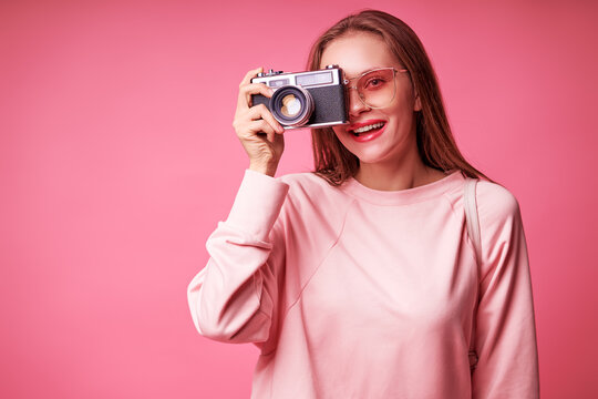 Traveler and photographer. Studio portrait of pretty young girl holding photocamera. Pink blackground.