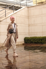 Portrait shooting of a stylish girl with pink hair. Beige shades. Trends of spring and summer 2023. Beige trench cloak with white t-shirt and beige pants. Black small belt bag