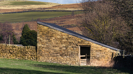 An old stone barn nestles in the corner of a field overlooked by the moors in West Yorkshire