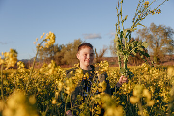 a child stands in a yellow field of flowers and holds a flower