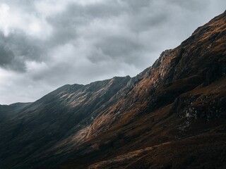 Fototapeta premium Horizontal view of the rocky mountains of Glencoe, Scottland under a clouded gray sky