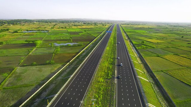 orbit aerial drone shot of new delhi mumbai jaipur express elevated highway showing six lane road with green feilds with rectangular farms on the sides