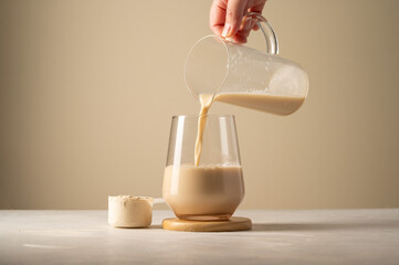 Protein powder and drink. Pouring chocolate drink in a glass.