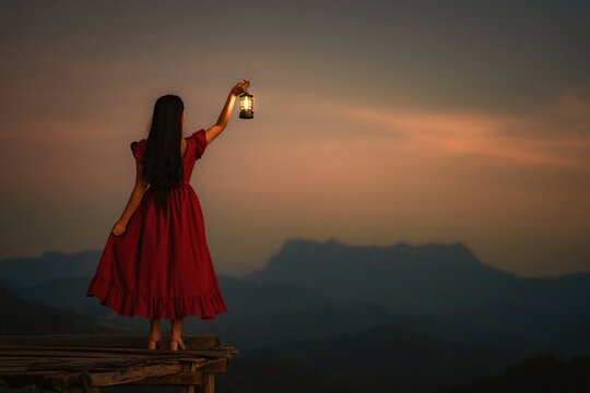 A woman standing with a lantern in the dark night on the mountain.