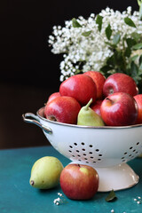 Red apples on black background. Vibrant colors of fresh seasonal fruit. Apples in a colander. White flowers and fruit still life. 