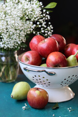 Red apples on black background. Vibrant colors of fresh seasonal fruit. Apples in a colander. White flowers and fruit still life. 