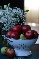 Naklejka na ściany i meble Red apples on black background. Vibrant colors of fresh seasonal fruit. Apples in a colander. White flowers and fruit still life. 