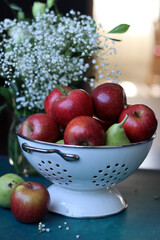 Red apples on black background. Vibrant colors of fresh seasonal fruit. Apples in a colander. White flowers and fruit still life. 