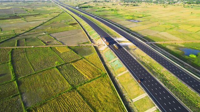 Pan up aerial drone shot showing six lane delhi jaipur surat vadodara mumbai highway passing straight through square green farms on outskirts