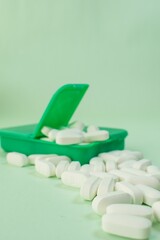 Vertical closeup shot of white pills in a green pillbox on a white background