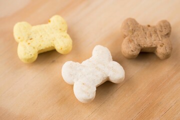 High angle closeup shot of three small colorful bone shaped pet cookies on a brown table
