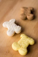 Foto auf Alu-Dibond Vertical high angle closeup shot of three small colorful bone shaped pet cookies on a brown table © Nicolas Ospina/Wirestock Creators
