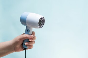 Closeup shot of a hand holding a blue hair dryer in front of a blue background
