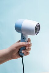 Vertical closeup shot of a hand holding a blue hair dryer in front of a blue background