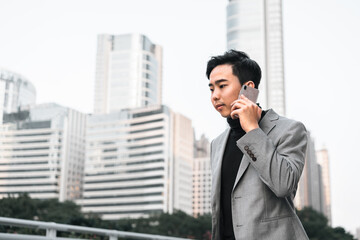 Asian businessman is making a phone call outdoors in the city. 