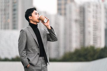 Asian businessman is drinking take away coffee outdoors in the city. 