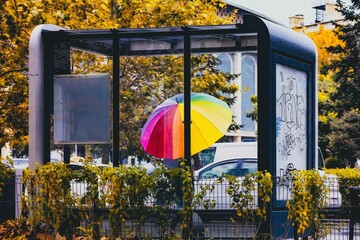 Person with rainbow umbrella waiting in bus station in autumn
