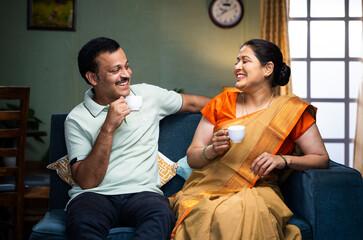 Happy smiling couple having tea or coffee while talking each other at home during morning - concept...