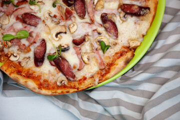 Pizza with mini sausages, bacon, meat, mushrooms and cheese. Thin homemade Italian pizza. Food background. Plate top view
